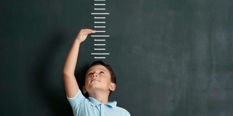 Child in front of blackboard with one hand above his head to indicate his future growth